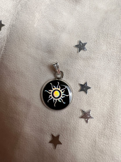 Ein 14mm runder Edelstahl Anhaenger mit schwarzem Hintergrund und einem Sonne Symbol welches in der Sonne in verschiedenen Farben schimmert
