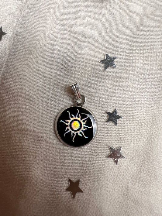 Ein 14mm runder Edelstahl Anhaenger mit schwarzem Hintergrund und einem Sonne Symbol welches in der Sonne in verschiedenen Farben schimmert