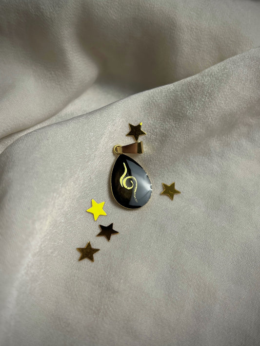Vergoldeter Edelstahl Anhänger mit einem schwarzen Hintergrund, in Tropfenform und einer goldenen Zwillingsflamme als Symbol 